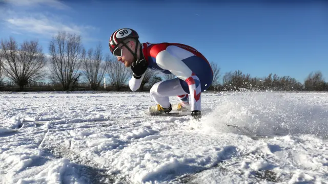 A man wearing red, white and blue clothing and a helmet skates on the ice in the sun