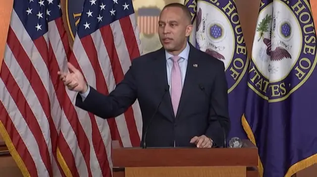 Hakeem Jeffries, Minority Leader of the US House of Representatives, speaks in Congress. He is wearing a suit and standing in front of two US flags and two emblems of the US House