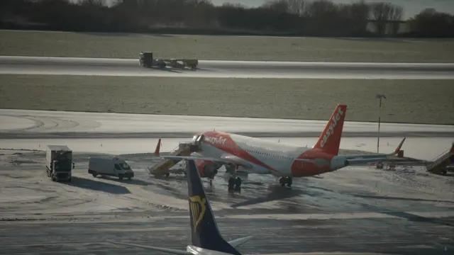An EasyJet plane waiting on the tarmac, snow dusting the ground as a tractor operates in the background