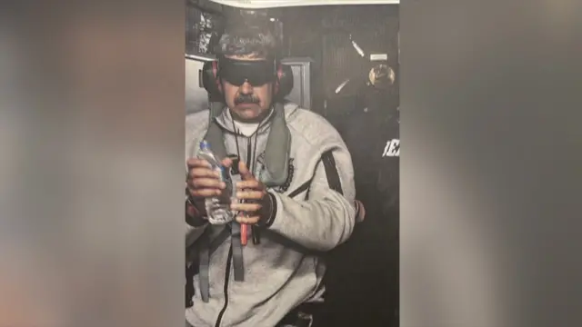 Nicolás Maduro shown after his arrest, wearing headphones and a blindfold, grey zipped jumper