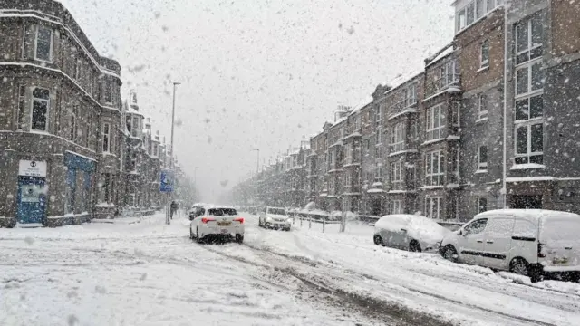 Cars travel down a snow-covered residential road