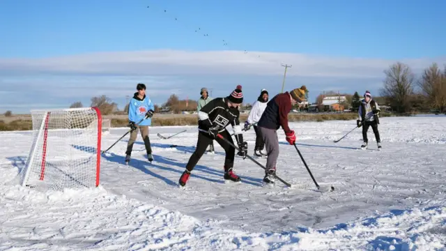 A group play ice hockey on a frozen filed in Cambridgeshire
