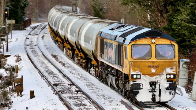 A yellow freight train drives along snowy tracks