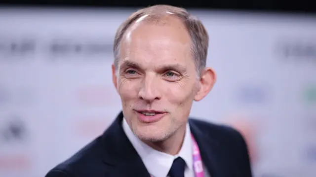 A headshot of Thomas Tuchel smiling while wearing a black suit