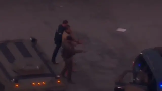 A man is escorted by two officers from an armoured police vehicle