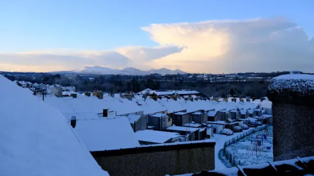 Snow covered roofs can be seen in front of snowy peaks in Wales