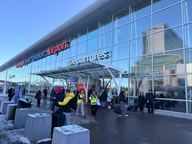 Travellers with bags waiting outside the terminal at John Lennon Airport in Liverpool