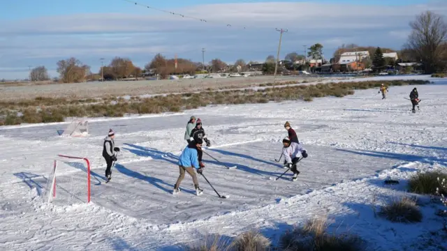 Six people play ice hockey on a frozen field