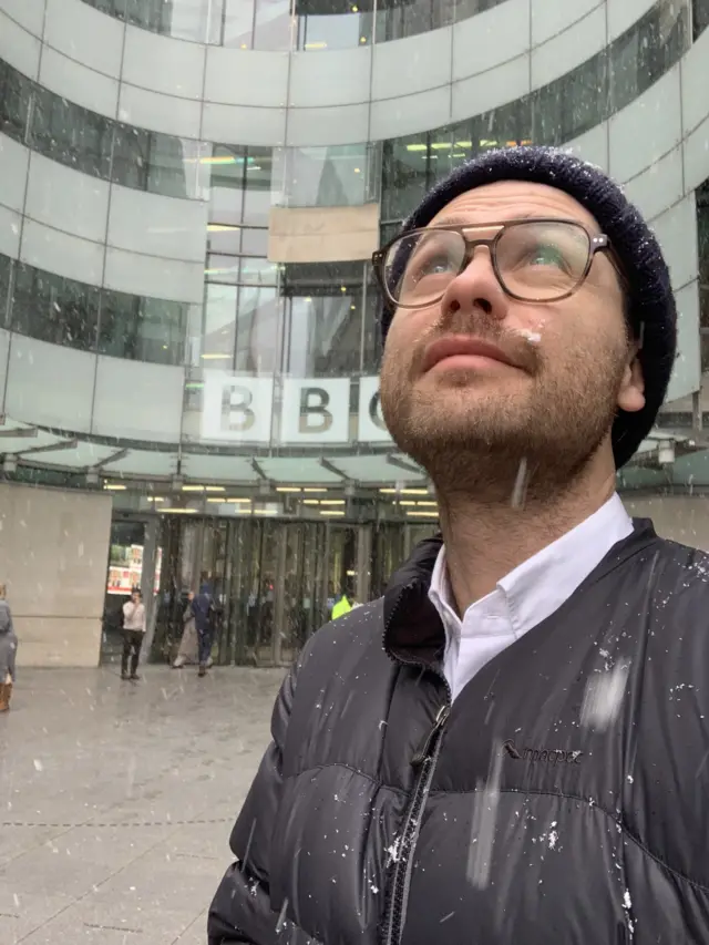 A man looks very happy in the snow outside of the BBC building