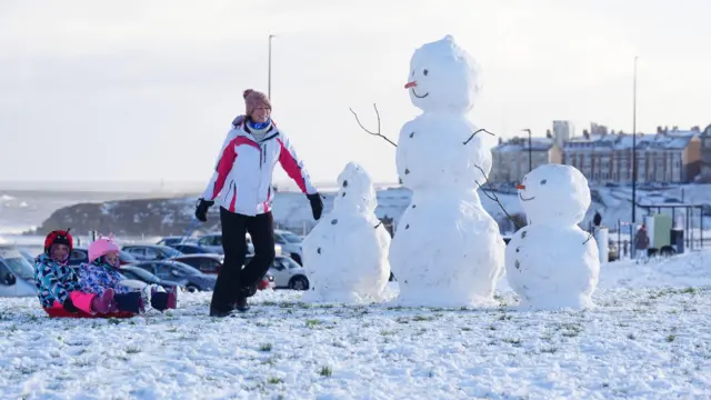 A woman pulls along two children on a sledge by snowmen earlier this week at Tynemouth the North East of England.