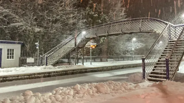 A snow covered train station with a bridge over the railway line