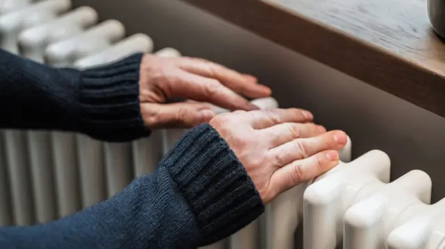 A pair of hands in a jumper with long blue sleeves held on top of a white radiator