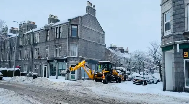 A yellow digger clears snow on a street corner