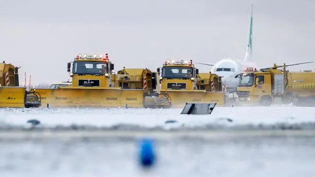 Trucks work to clear snow in front of a plane at Amsterdam airport