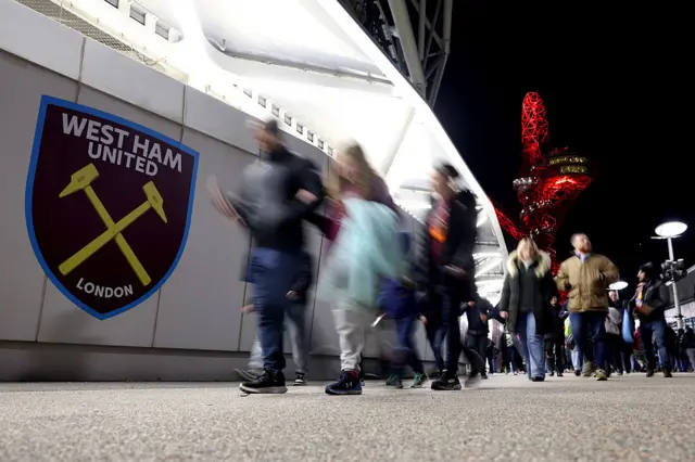 West Ham badge on wall with people walking past