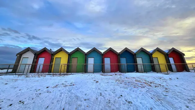 Colourful beach huts surrounded by snowy landscape and cloudy sky
