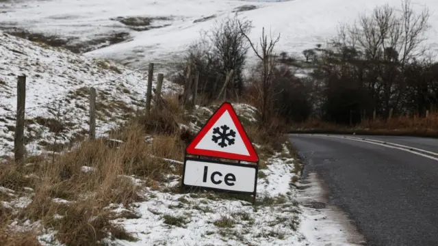 An ice warning sign on a snowy roadside