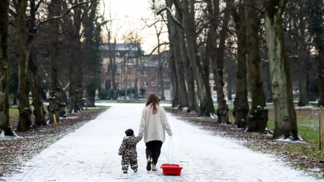 A woman walks with her child along a snow-covered path in Alexandra Park in Manchester, she is pulling a sledge