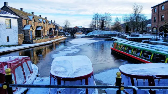 Boats covered in frost and snow on a partially frozen body of water in Brecon