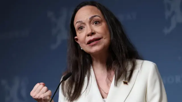 Machado wearing a white jacket and speaking at an event.