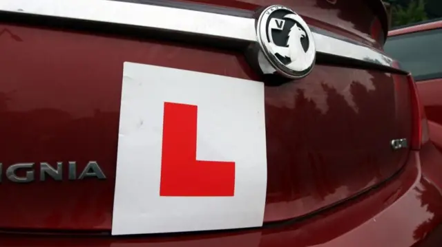 A learner sticker on the bumper of a red car