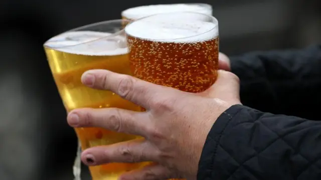 A close-up of a pair of hands carrying three pints of beer