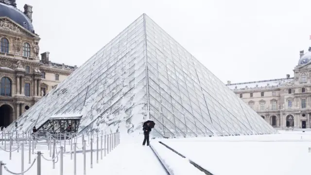 The Louvre Pyramid covered in slates of ice, with person standing on snow-covered floor