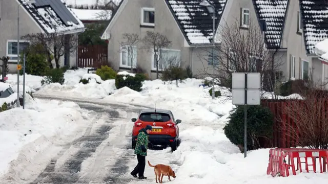 A car and dog walker on a heavily snowed in street in Drumoak, Scotland