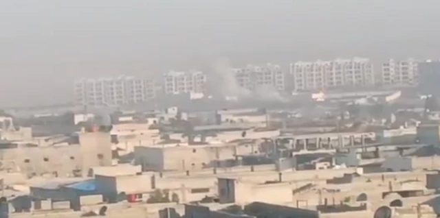 A plume of smoke rising near some high-rise buildings in the distance