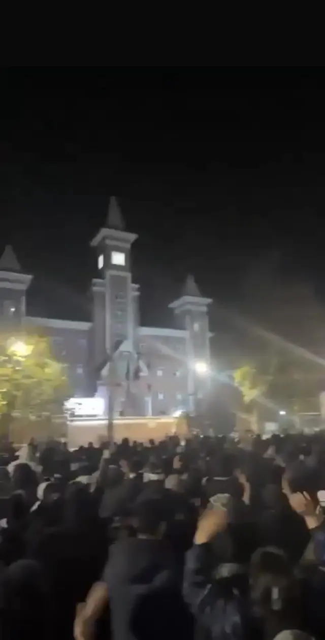 Crowds gather in a public square. Hundreds of people can be seen dressed in black.