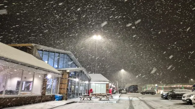 A snowy and windy car park outside a shop