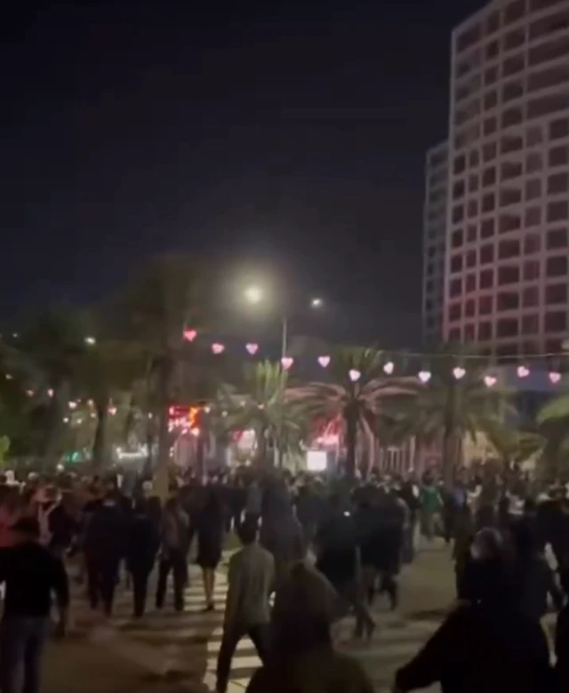 Crowds walk down a street in Kish Island with palm trees and lights seen in the background
