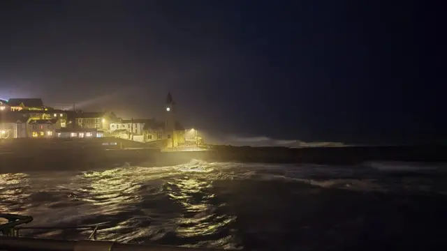 Waves at Porthleven in Cornwall dimly lit by street lights with houses in the distance