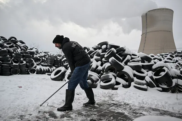 A worker shovels snow in front of a pile of discarded tires covered in snow at a tyre recycling factory near the town of Obilic.