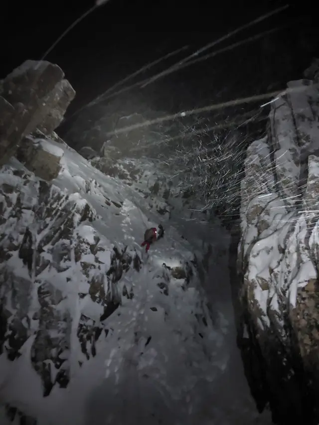 Two hikers can be seen up a rocky crag in the snow