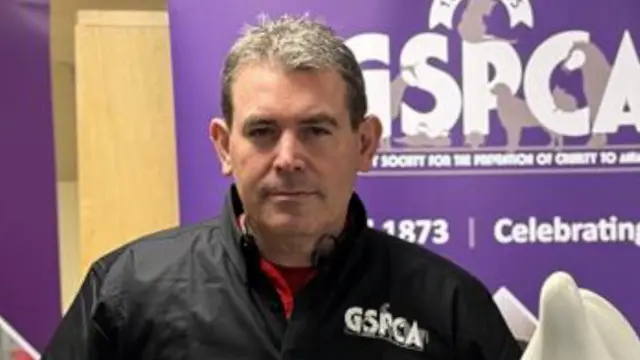 Steve Byrne, wearing a GSPCA coat. He is stood in front of a purple GSPCA sign.