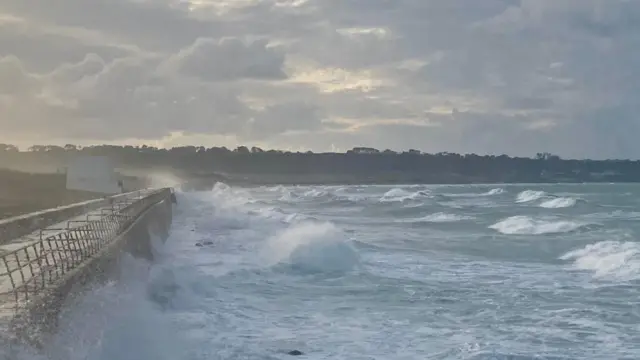 St Ouen’s Bay in Jersey. There are big waves. The sea is blue. There are grey clouds.