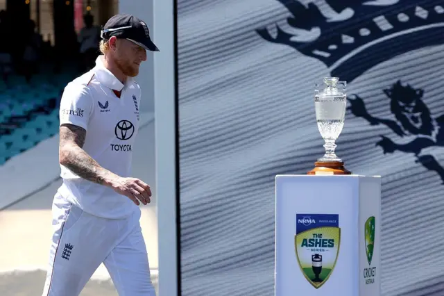 Ben Stokes walks past the Ashes trophy