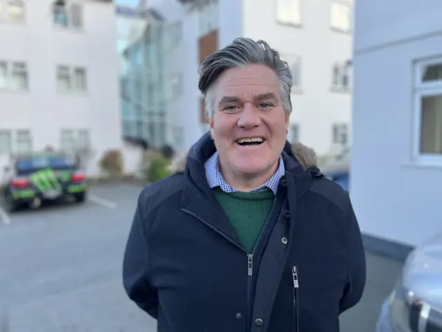 A picture of John Merrien - who is wearing a green jumper and navy coat.