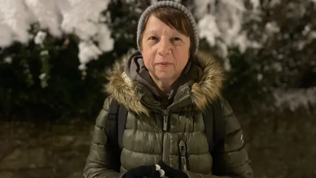 Julia Ward - a woman wearing a grey hat, large green coat and black gloves - stands on a snow-covered pavement.