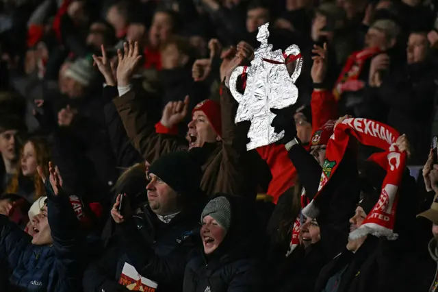 Wrexham fans celebrate and hold a tinfoil trophy in the air