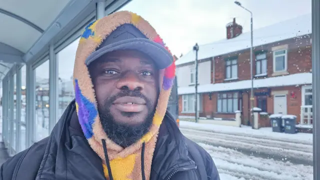 A man with cap wearing a hoodie stood in the snow at Alfreton Bus Station