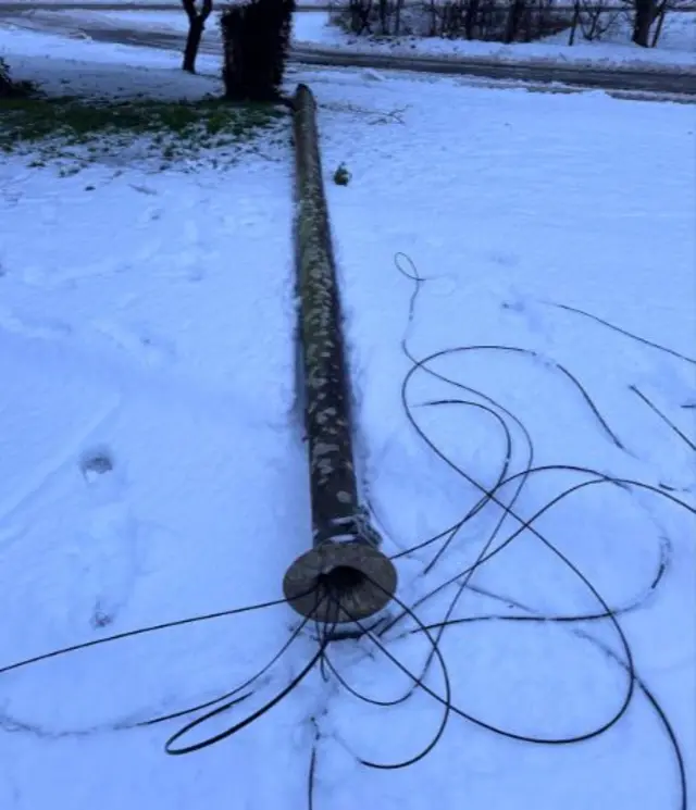 A large pole lies on the snowy ground, with wires coming off it