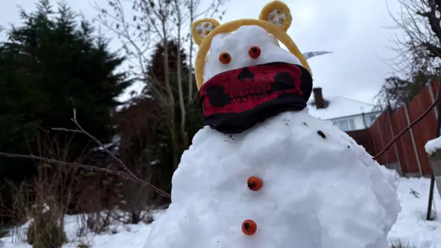 A snowman wearing a Pudsey headband and a black balaclava with an image of a red skull.