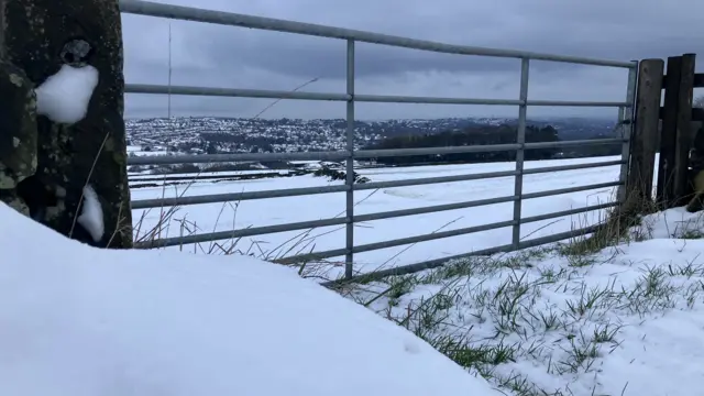 Snow covered fields and hills visible through a gate in the countryside