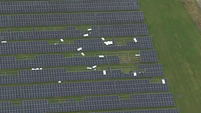 Rows of solar panels in a green field. Some of the panels have been disrupted and have blown away.
