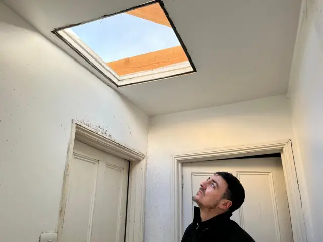 A man looks up at the hole in the roof above his head