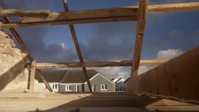 A view from inside the home looking out of the roof shows a large hole above.