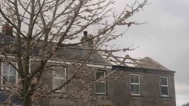 A house with its roof blown off on one side is seen from below