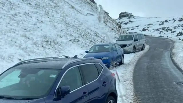 A row of cars parked on the side of a snowy mountain road